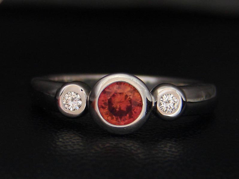This untreated Padparadscha sapphire comes from Umba Valley, Tanzania. The pad sapphire weight is .68 cts 5.1 mm round and two 2.0 mm round diamonds. Set in a 14k white gold. The clarity of the pad is VS. The diamonds are g-h color and VS in clarity.<br />Price: 590$